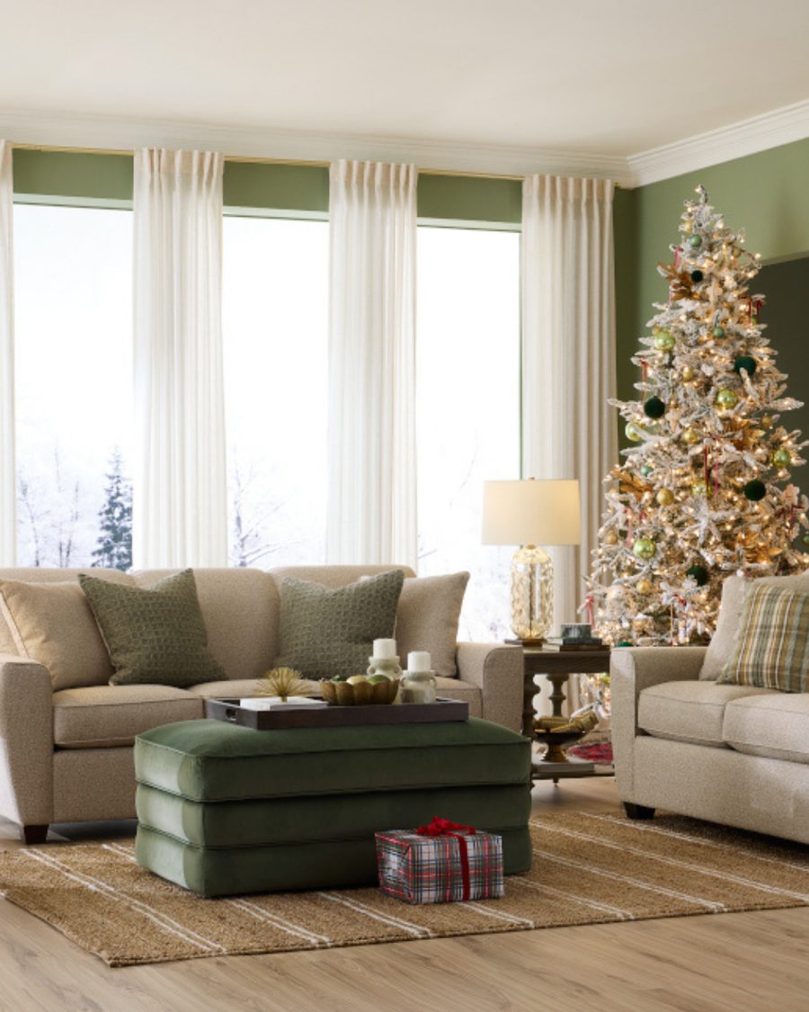 Sage green living room with cream sofas, a green velvet ottoman and a flocked Christmas tree