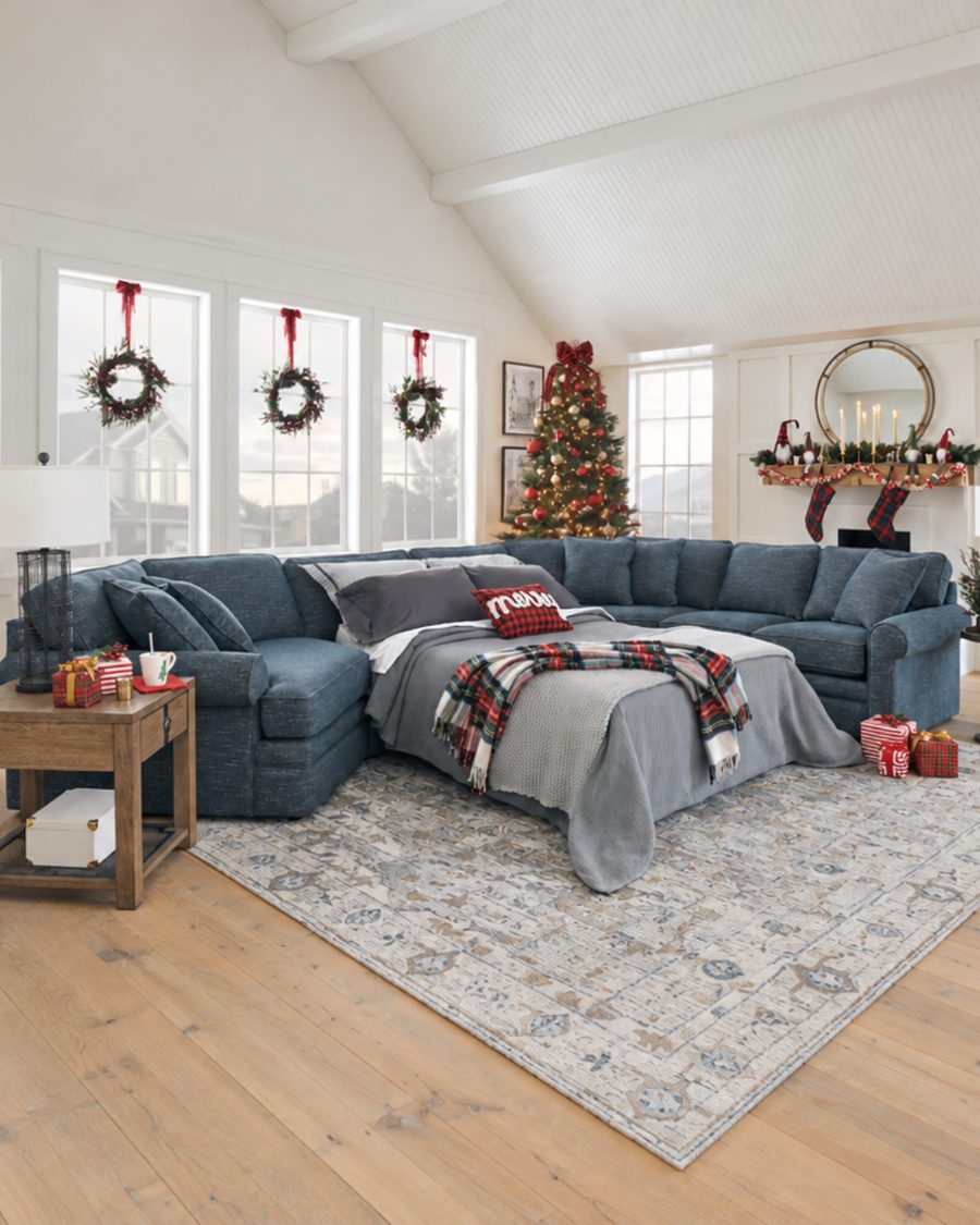 Blue sleeper sectional opened into a made bed with a plaid throw beside a Christmas tree