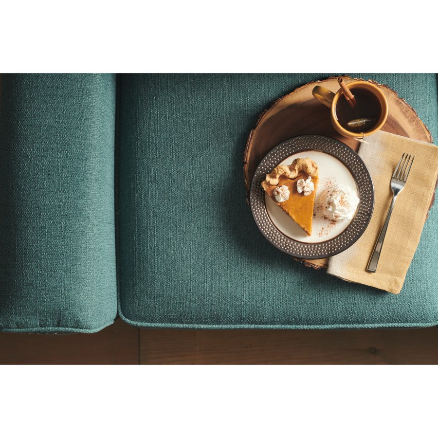 Pumpkin pie and spiced cider on a wood tray resting on teal sofa fabric