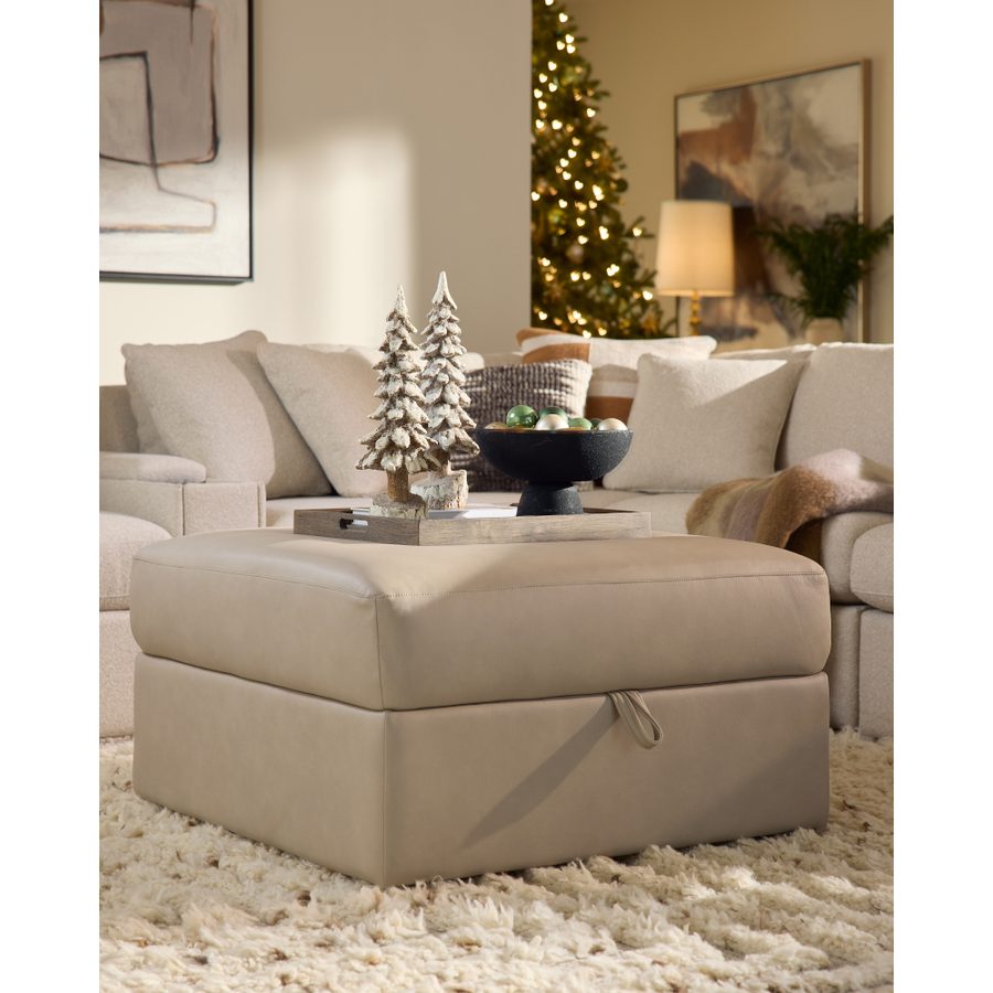Cream sectional and storage ottoman with frosted mini trees and a lit Christmas tree